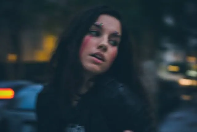 Marina Alves, cantora indie, em retrato noturno com luzes da cidade desfocadas ao fundo