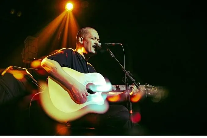 Vocalista da Rua de Baixo tocando violão sob luz de palco alaranjada